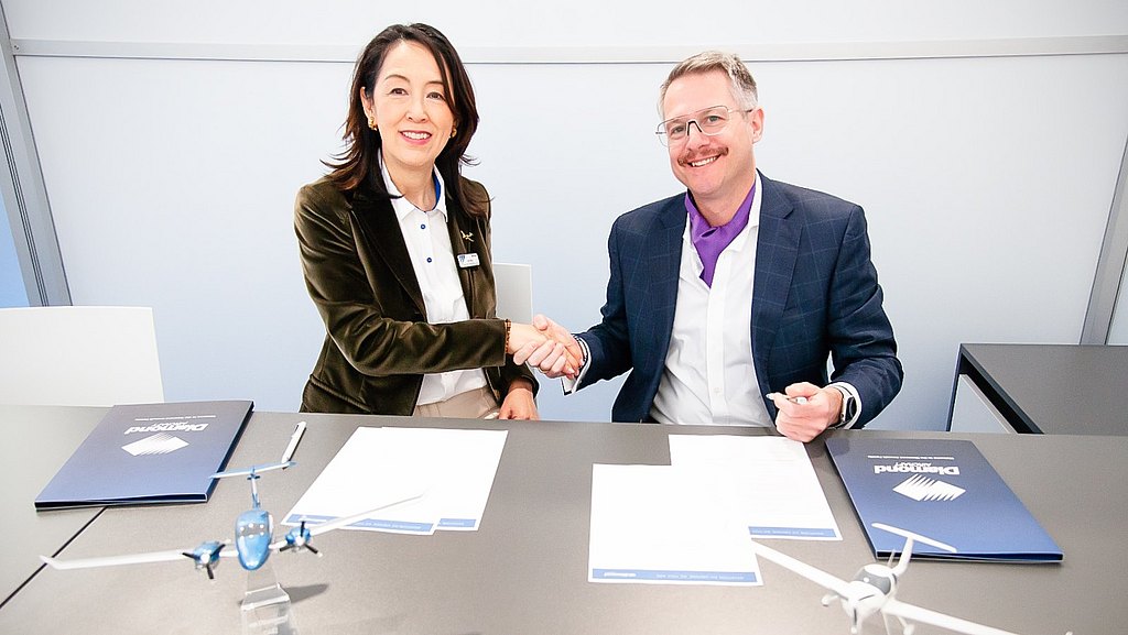 Women and men sitting at a table, shaking hands while signing a document.