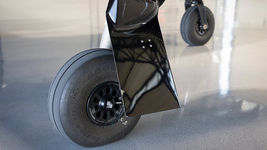 The image highlights a robust aircraft tire mounted on a black wheel, reflecting light against a smooth, glossy floor.