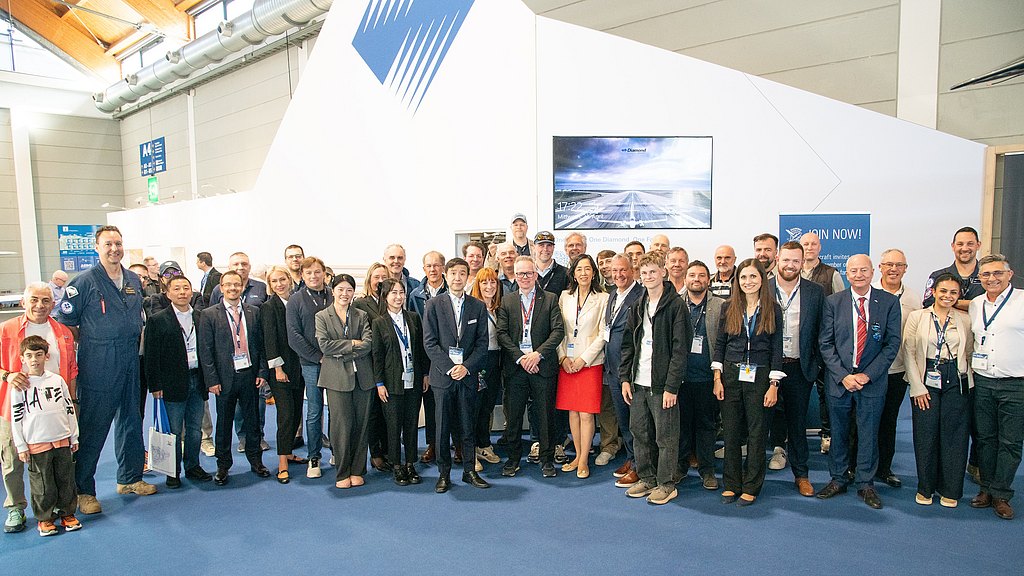 A diverse group of professionals gathers at an event, smiling and posing together in a modern exhibition space.