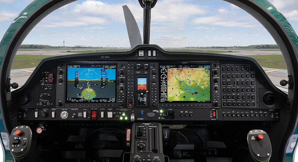 Inside the aircraft cockpit, two large digital displays show flight metrics and navigation maps, while controls are neatly arranged.