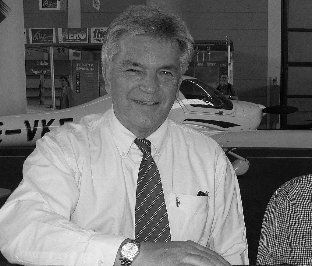 A smiling man with gray hair is posing in front of an airplane.