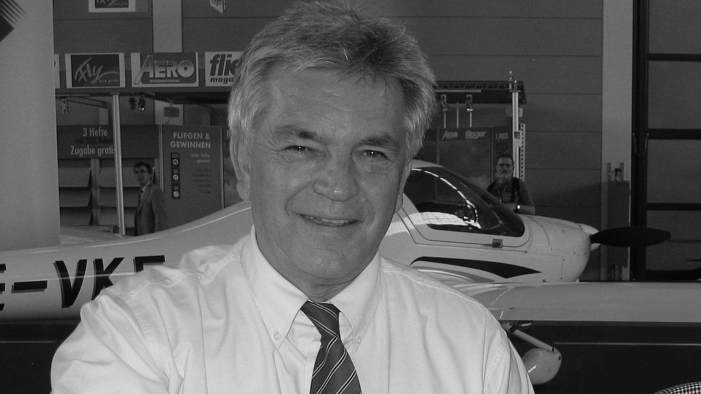 A smiling man with gray hair is posing in front of an airplane.