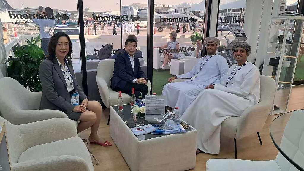 Inside a sleek exhibition space, four people are gathered around a coffee table, showcasing a collaborative atmosphere.