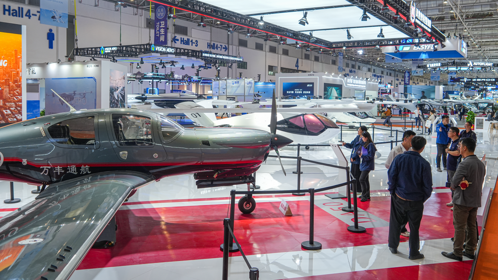 Visitors gather around a striking DA50 RG aircraft at an aviation event, with multiple planes and informative displays in the background.