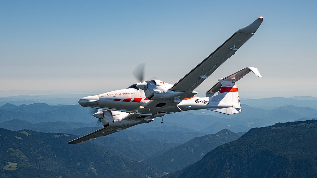 A DA62 MPP aircraft with a sleek design flies over a mountainous landscape, showcasing its distinctive markings.