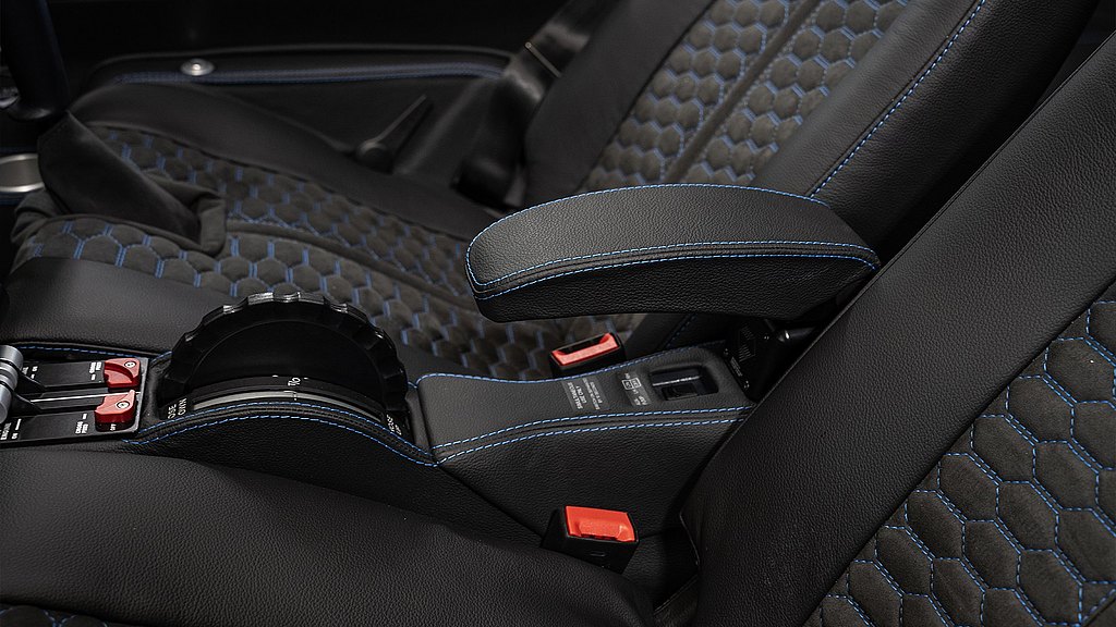 A close-up view of a sleek aircraft interior featuring black leather seats with blue stitching and a central armrest.