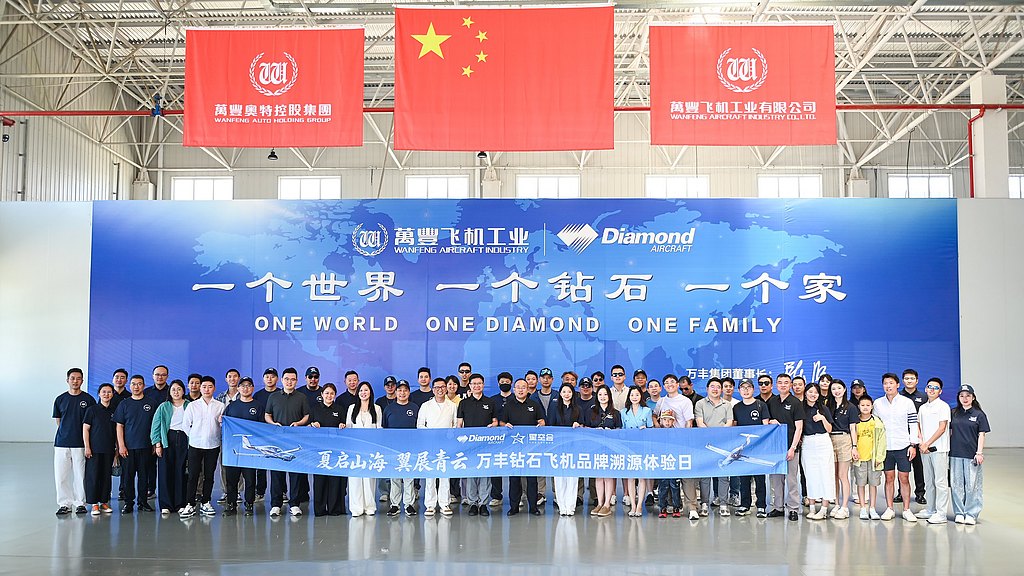 A large group of people stands together in a spacious indoor setting, holding a banner that promotes unity and teamwork.