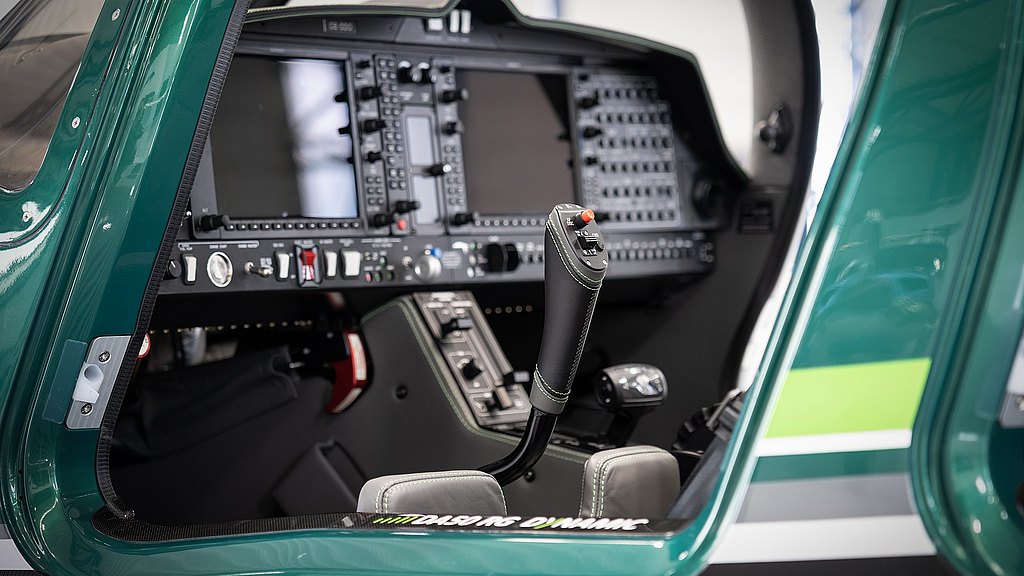 The cockpit features a sleek leather control stick with various buttons, surrounded by an array of advanced flight instruments.