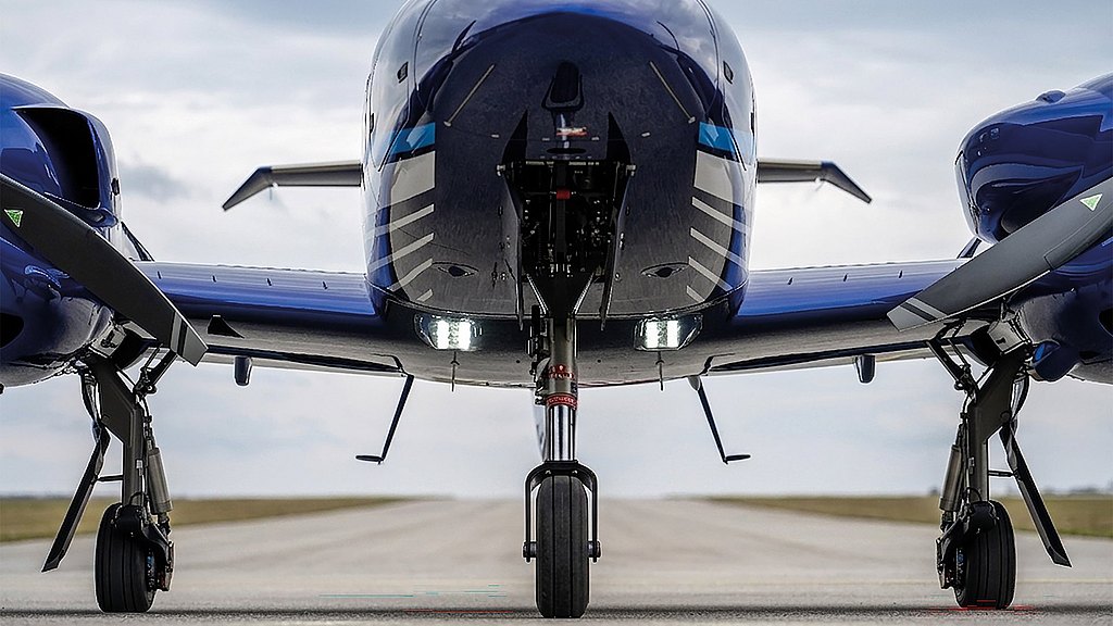A blue DA42 aircraft is positioned on the tarmac, showcasing its landing gear and bright taxi lights against a cloudy sky.