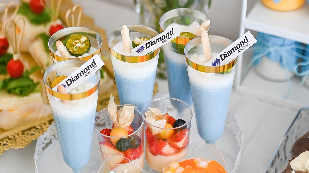 A beautifully arranged dessert table featuring colorful layered drinks and fresh fruit cups, surrounded by vibrant flowers.
