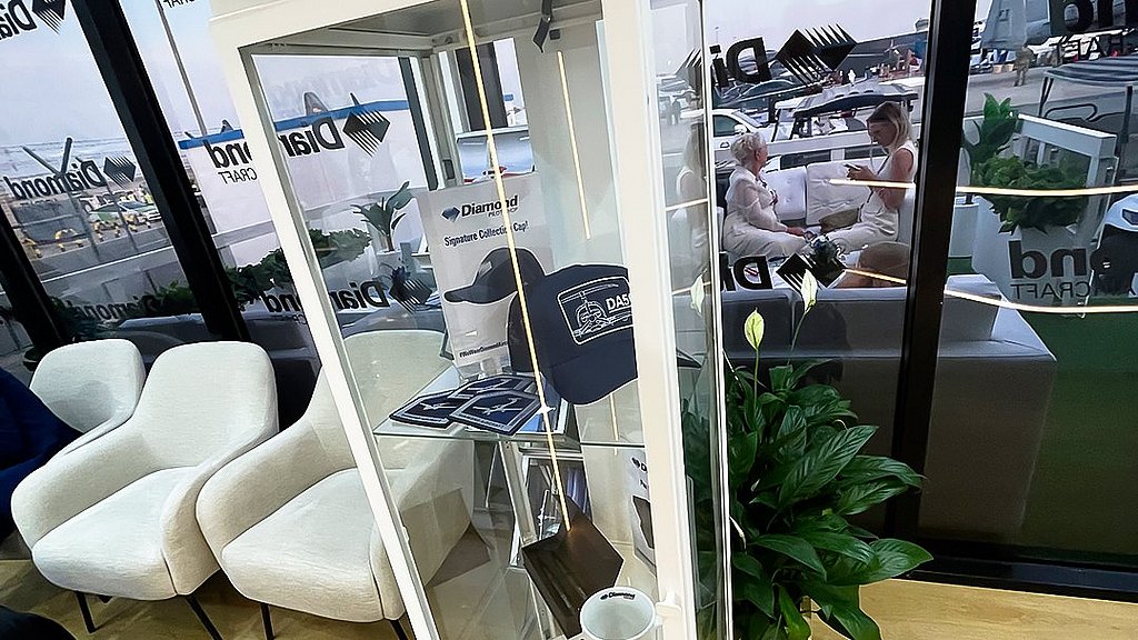 A glass display case showcases branded merchandise, including a cap, mug, and brochures, in a modern lounge setting.