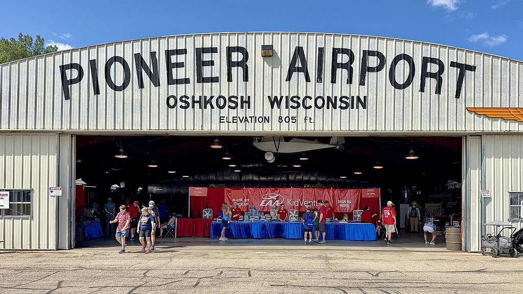 A bustling scene at Pioneer Airport in Oshkosh, featuring families engaging in activities at the EAA KidVenture event.