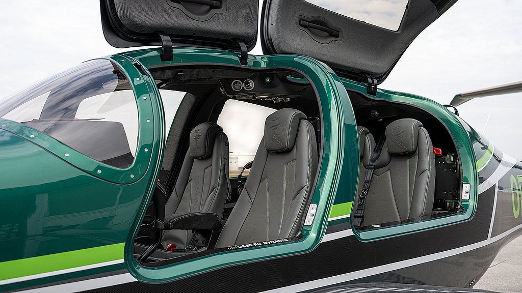 The interior of a sleek green DA50 RG aircraft features two open doors, revealing modern gray seats with green stitching.