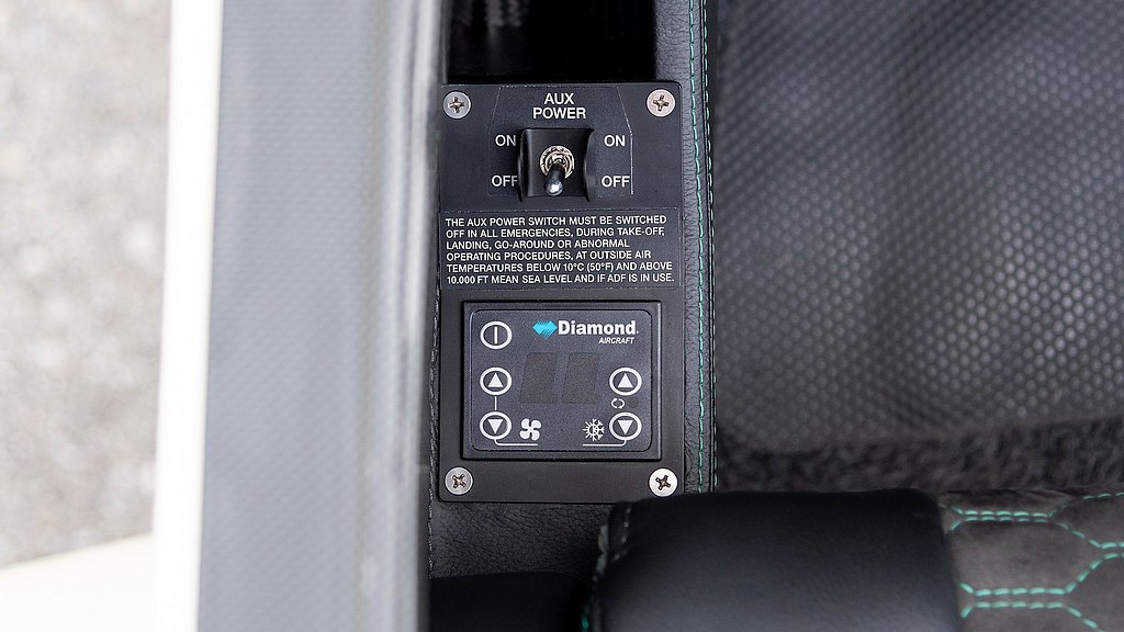 A close-up view of an aircraft control panel featuring an AUX power switch and temperature control buttons.