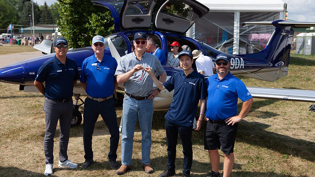 A group of five men stands proudly in front of a small aircraft, celebrating a special moment at an aviation event.
