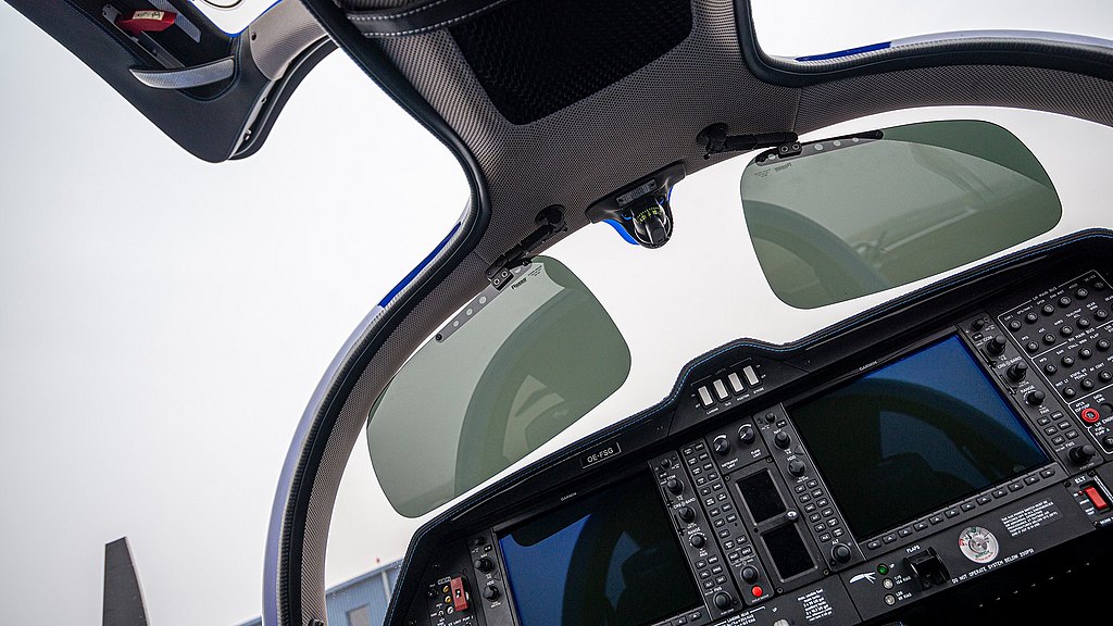 A close-up of an aircraft cockpit shows sleek sun visors and an array of buttons and displays, emphasizing pilot controls.