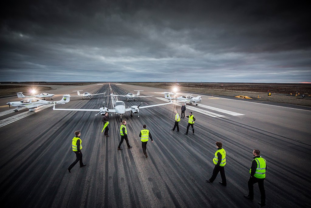People with safety vests walking in front of DA42, DA40 and DA20 fleet on the runway.