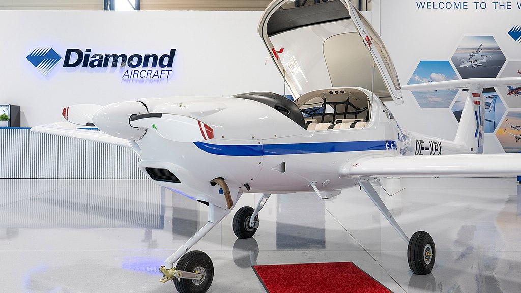 In a stylish aviation showroom, a white DA20i Katana plane with a blue accent is prominently displayed, showcasing its elegant design and features.