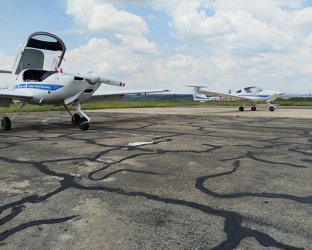 Two DA20 aircraft are parked on a cracked runway under a partly cloudy sky, showcasing their sleek designs.
