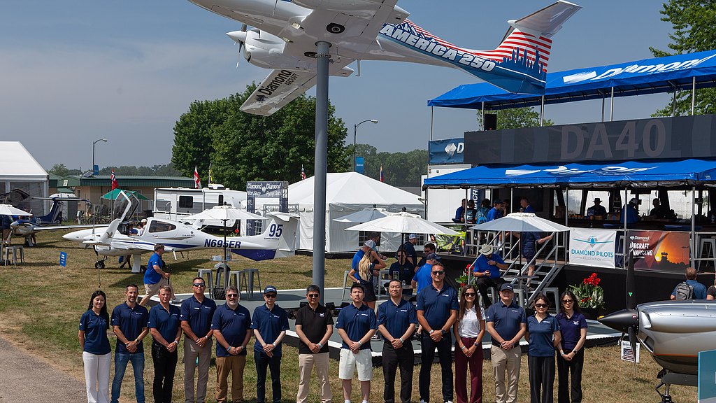 A diverse group of people stands together in front of aircraft at an aviation event, showcasing camaraderie and teamwork.