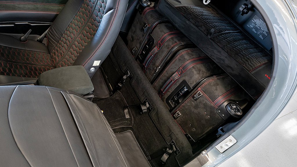 A sleek aircraft interior features luxurious black leather seats with red stitching, showcasing neatly arranged luggage in the back.