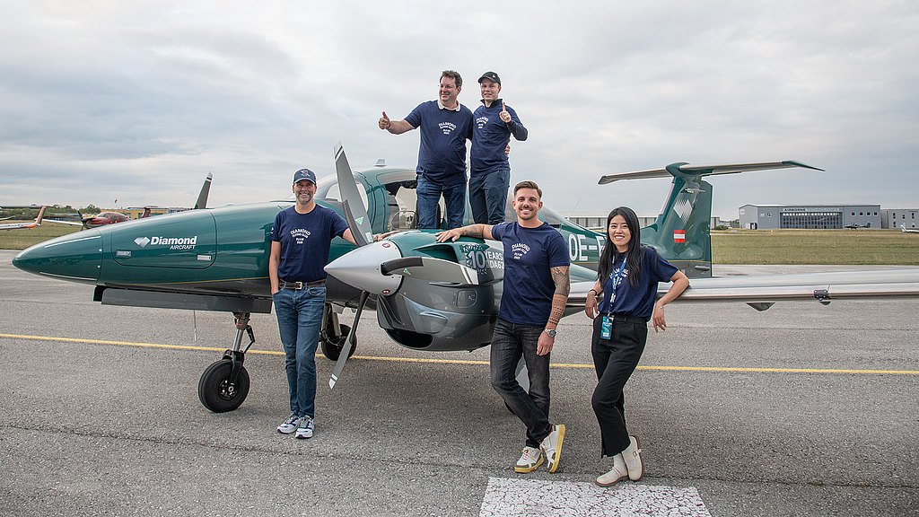 Four men and a woman standing next to a green DA62 on the apron. 