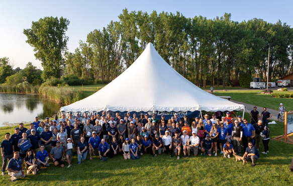 Large group of people standing in front of a tent at a lake.
